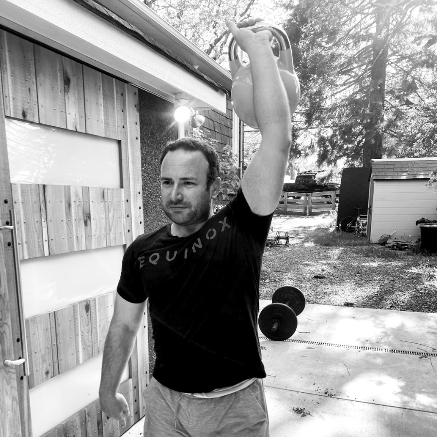 Black and white photo of a man lifting a weight outside.