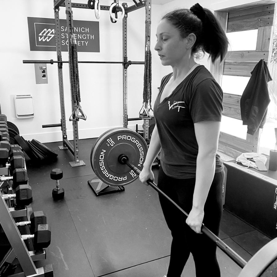 Black and white photo of a woman lifting a bar with weights on it in a gym.