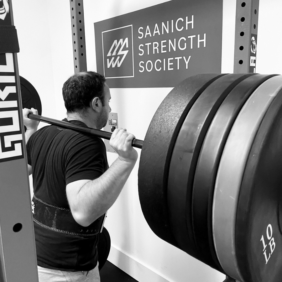 Black and white photo of a man lifting a bar with four large weights on it.